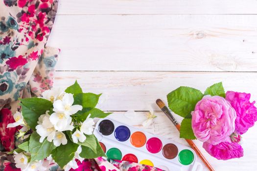 Desk of creative worker. Paints, brush and flowers. Top view background