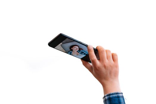 Close-up of the hand of a young red-haired girl taking a selfie with her mobile phone. The selfie can be seen on the mobile screen. White background.