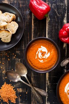 Delicious pumpkin soup with heavy cream on dark rustic wooden table with red bell pepper, bread toasts, lentil. Top view