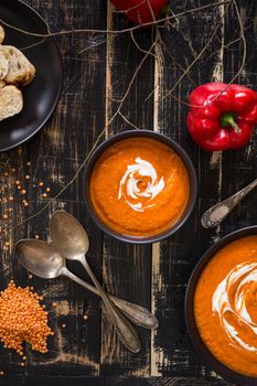 Delicious pumpkin soup with heavy cream on dark rustic wooden table with red bell pepper, bread toasts, lentil and autumn branches. Top view