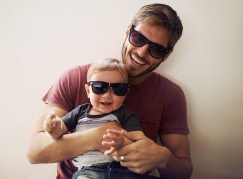 A young father and his infant son wearing matching sunglasses and laughing.