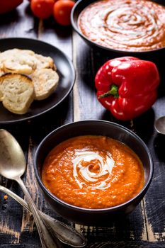 Delicious pumpkin soup with heavy cream on dark rustic wooden table with red bell pepper, bread toasts, lentil, tomatoes