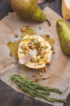 Delicious beautiful baked camembert with fork. Cheese with honey, walnuts, herbs and pears