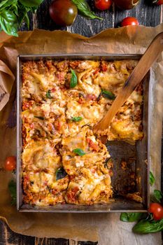 Top view of a delicious traditional italian lasagna made with minced beef bolognese sauce topped with basil leafs served on a rustic dark wooden table
