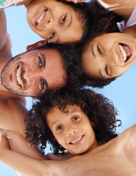A family of four in swimwear smiling against a bright sky.