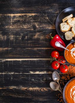 Delicious pumpkin soup with heavy cream on dark rustic wooden table with red bell pepper, toasts. Autumn/Halloween/Thanksgiving day background. Top view. Space for text