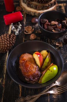 Roasted duck breast with golden crispy skin served with baked apples and chestnuts. Served on a ceramic black plate over rustic dark wooden table with a deer napkin ring and candles. Close up