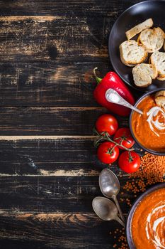 Delicious pumpkin soup with heavy cream on dark rustic wooden table with red bell pepper, toasts. Autumn/Halloween/Thanksgiving day background. Top view. Space for text