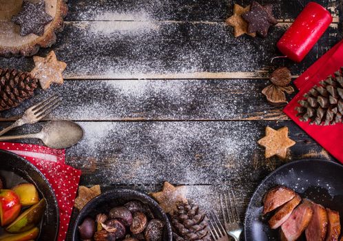 Christmas dinner table served with roasted duck breast, baked apples, chestnuts, gingerbread cookies. Decorated with red candles, pine cones, snow. Christmas background with free space for text. Xmas concept