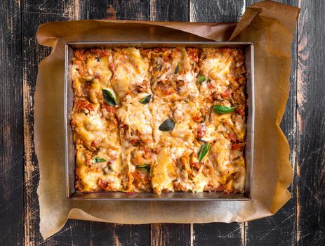 Top view of a delicious traditional italian lasagna made with minced beef bolognese sauce topped with basil leafs served on a rustic dark wooden table