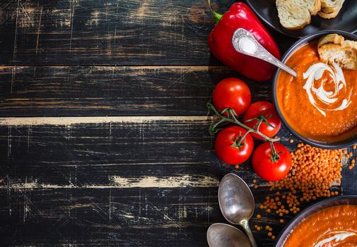 Delicious pumpkin soup with heavy cream on dark rustic wooden table with red bell pepper, toasts. Autumn/Halloween/Thanksgiving day background. Top view. Space for text