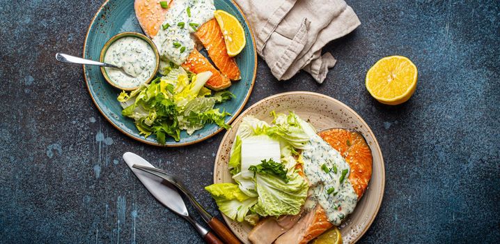 Healthy food meal grilled salmon steaks with dill sauce and salad leafs on two plates on rustic concrete stone background table flat lay from above, diet healthy nutrition dinner
