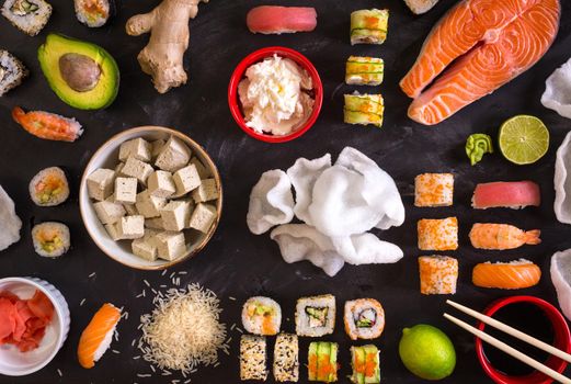 Set of traditional japanese food on a dark background. Sushi rolls, nigiri, raw salmon steak, rice, cream cheese, avocado, lime, pickled ginger (gari), raw ginger, wasabi, soy sauce, nori, сhopsticks. Asian food frame. Dinner party. Space for text....