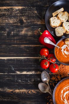 Delicious pumpkin soup with heavy cream on dark rustic wooden table with red bell pepper, toasts. Autumn/Halloween/Thanksgiving day background. Top view. Space for text