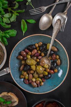 Table served with tapenade, mixed marinated olives (green, black and purple) in ceramic bowl and basil leaves. French provence appetizers and snacks. Close-up