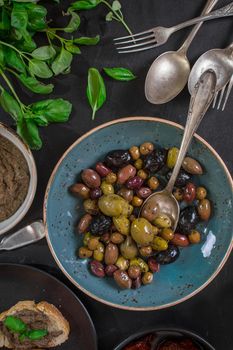 Table served with tapenade, mixed marinated olives (green, black and purple) in ceramic bowl and basil leaves. French provence appetizers and snacks. Close-up
