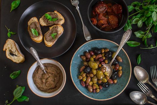 Table served with bread, tapenade, assorted olives, dried tomatoes in olive oil and basil. Dinner table with french provence appetizers and canapes