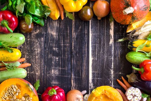 Fresh vegetables on a old rustic dark textured table. Autumn background. Healthy eating frame. Sliced pumpkin, zucchini, squash, bell peppers, carrots, onions, cut garlic, tomatoes, eggplant, corn cob, rucola and basil. Top view. Space for text