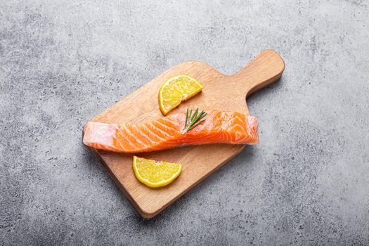 Raw salmon fish fillet with lemon wedges and rosemary on wooden cutting board on gray stone concrete rustic background kitchen table from above, healthy eating and diet