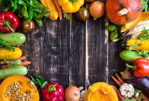 Fresh vegetables on a old rustic dark textured table. Autumn background. Healthy eating frame. Sliced pumpkin, zucchini, squash, bell peppers, carrots, onions, cut garlic, tomatoes, eggplant, corn cob, rucola and basil. Top view. Space for text