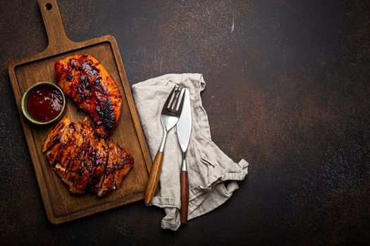 Grilled turkey or chicken marinated fillet with red sauce served and sliced on wooden cutting board on stone brown background from above, poultry breast barbecue space for text