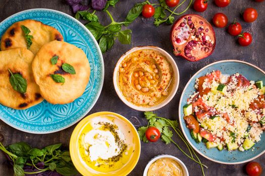 Table served with middle eastern traditional vegetarian dishes. Hummus, tahini, pitta, couscous salad and buttermilk dip with olive oil. Dinner party