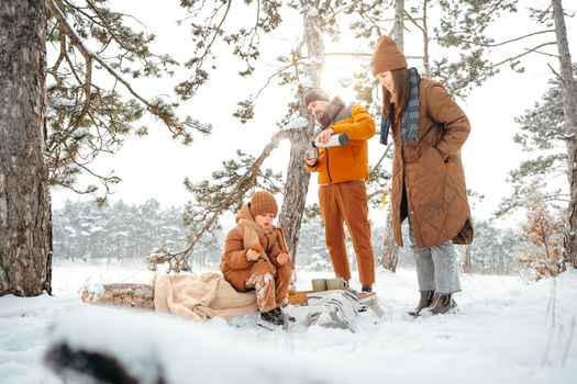 Happy family with cups of hot tea spending time together in winter forest, close up