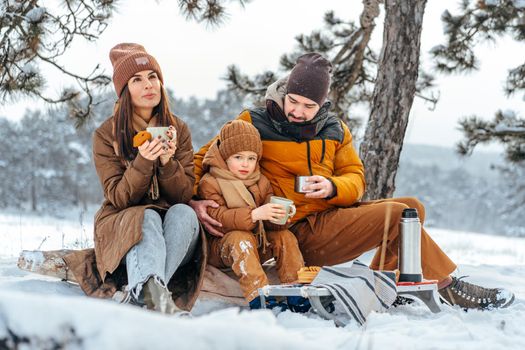 Happy family with cups of hot tea spending time together in winter forest, close up