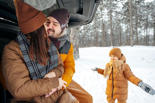 Lovely smiling couple sitting in car trunk in winter forest, close up