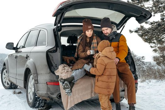 Winter portrait of a family sit on car trunk enjoy their vacation in snowy forest