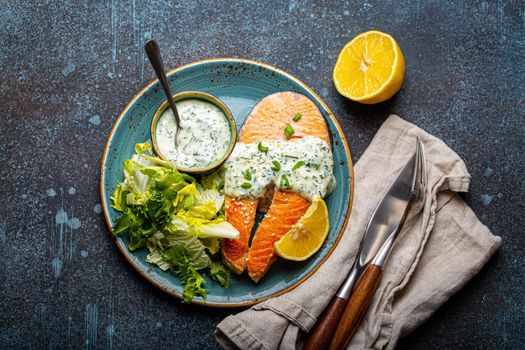 Healthy food meal cooked grilled salmon steaks with white dill sauce and salad leafs on plate on rustic concrete stone background table flat lay from above, diet healthy nutrition dinner