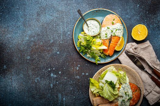 Healthy food meal grilled salmon steaks with dill sauce and salad leafs on two plates on rustic concrete stone background table flat lay from above, diet healthy nutrition dinner, space for text