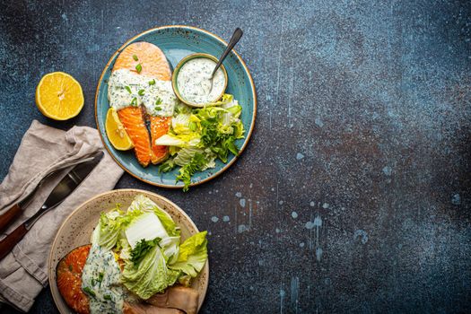 Healthy food meal grilled salmon steaks with dill sauce and salad leafs on two plates on rustic concrete stone background table flat lay from above, diet healthy nutrition dinner, space for text