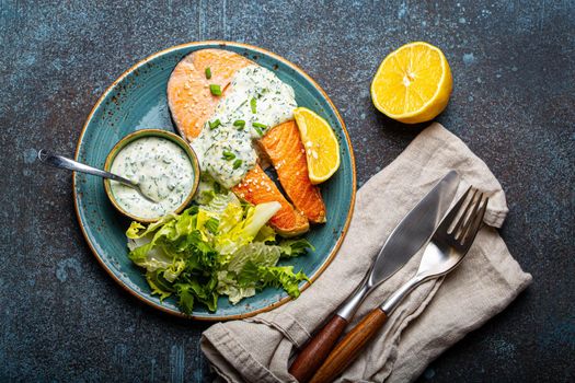 Healthy food meal cooked grilled salmon steaks with white dill sauce and salad leafs on plate on rustic concrete stone background table flat lay from above, diet healthy nutrition dinner