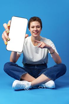 Happy woman shows blank smartphone screen against blue background, close up