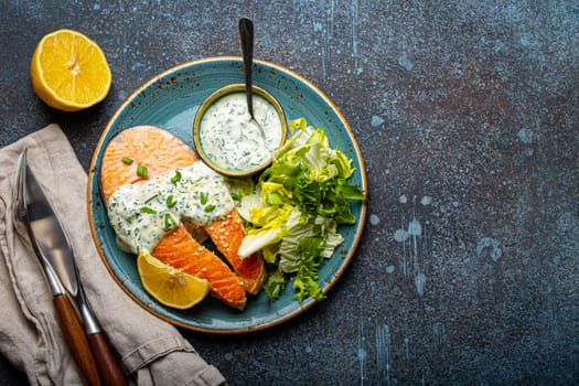 Healthy food meal cooked grilled salmon steaks with white dill sauce and salad leafs on plate on rustic concrete stone background table flat lay from above, diet healthy nutrition dinner copy space