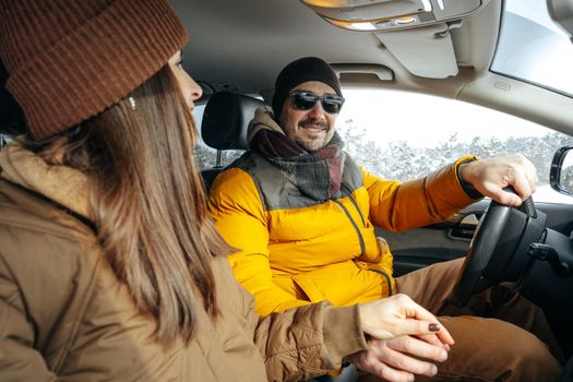 Family couple sitting in car in winter clothes iin snow forest, close up