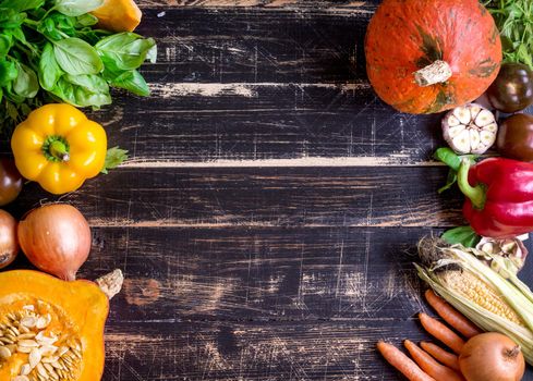 Fresh vegetables on a old rustic dark textured table. Autumn background. Healthy eating frame. Sliced pumpkin, bell peppers, carrots, onions, cut garlic, tomatoes, rucola and basil. Top view. Space for text