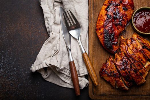 Grilled turkey or chicken marinated fillet with red sauce served and sliced on wooden cutting board on stone brown background from above, poultry breast barbecue space for text