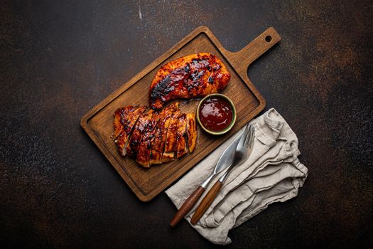 Grilled turkey or chicken marinated fillet with red sauce served and sliced on wooden cutting board on stone brown background from above, poultry breast barbecue