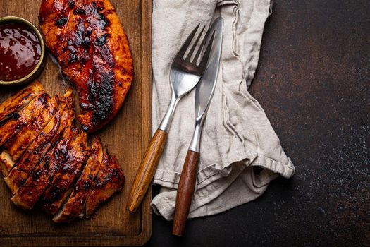 Grilled turkey or chicken marinated fillet with red sauce served and sliced on wooden cutting board on stone brown background from above, poultry breast barbecue space for text