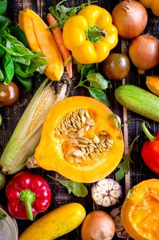 Fresh vegetables scattered on a old rustic dark textured table. Autumn background. Healthy eating. Sliced pumpkin, zucchini, squash, bell peppers, carrots, onions, cut garlic, tomatoes, eggplant, corn cob, rucola and basil. Top view