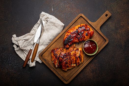 Grilled turkey or chicken marinated fillet with red sauce served and sliced on wooden cutting board on stone brown background from above, poultry breast barbecue