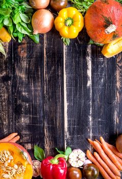 Fresh vegetables on a old rustic dark textured table. Autumn background. Healthy eating frame. Sliced pumpkin, bell peppers, carrots, onions, cut garlic, tomatoes, rucola and basil. Top view. Space for text