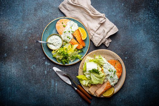 Healthy food meal grilled salmon steaks with dill sauce and salad leafs on two plates on rustic concrete stone background table flat lay from above, diet healthy nutrition dinner