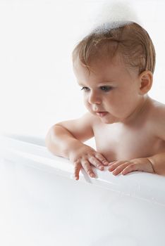 An adorable baby boy standing in the bathtub.