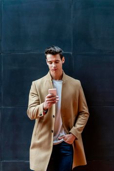 Cheerful man leaning against wall in the city using smartphone