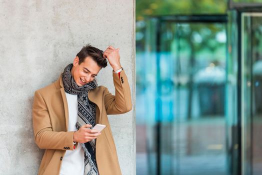 Cheerful man leaning against wall in the city using smartphone