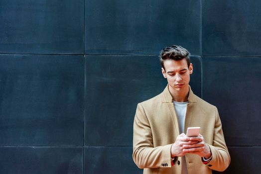 Cheerful man leaning against wall in the city using smartphone