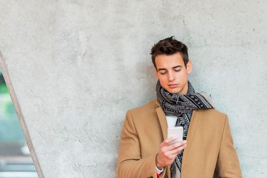 Cheerful man leaning against wall in the city using smartphone